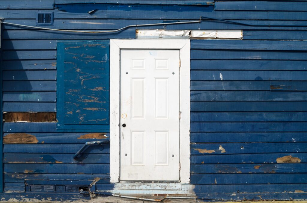 Rustic run down shabby building house with blue wooden siding and white door in disrepair