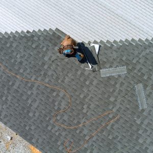 A asphalt shingles installation on the roof roofer is nailing asphalt shingles to roofing constructi